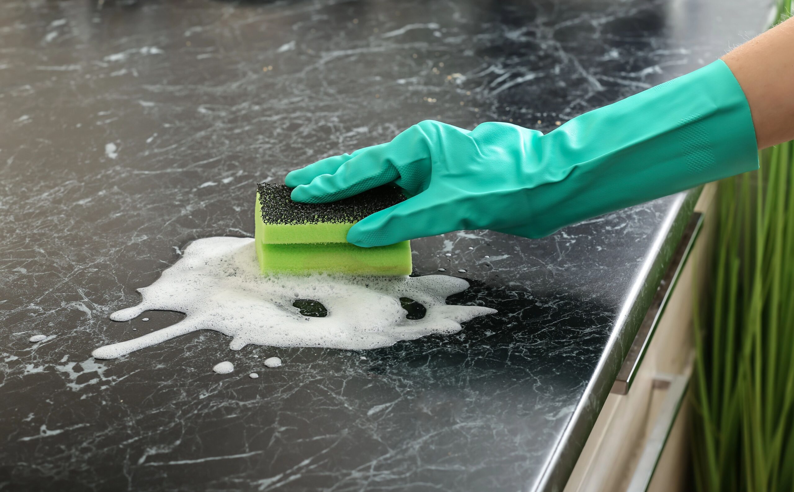 Hand mit Handschuh reinigt Oberfläche mit Schwamm.